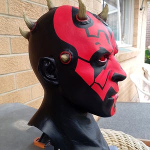 May include: A red and black Darth Maul mask with horns. The mask is made of a hard plastic and has a detailed paint job.