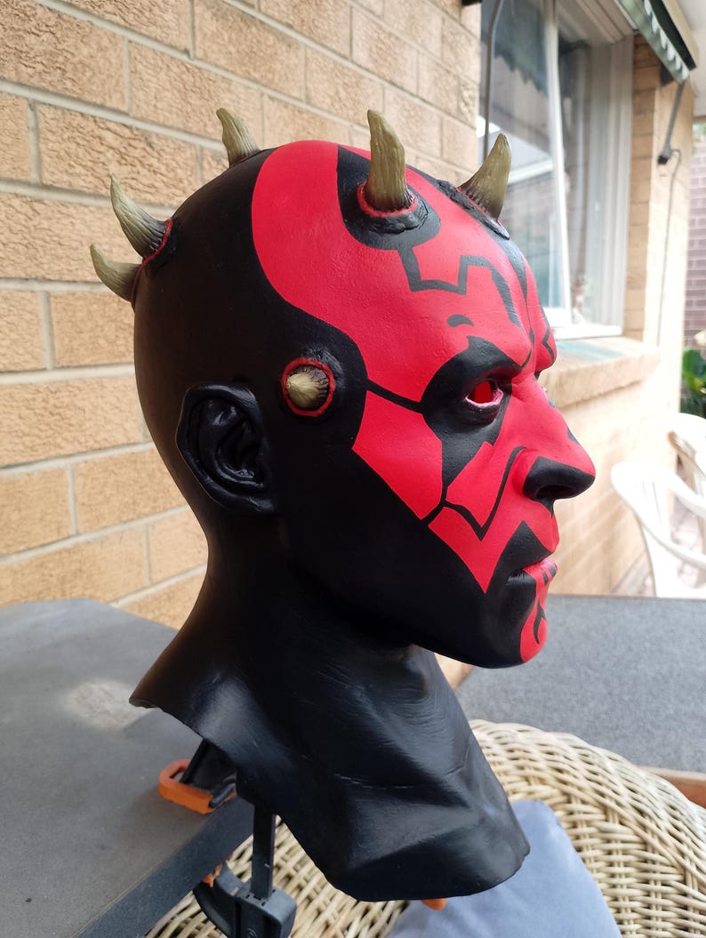 May include: A red and black Darth Maul mask with horns. The mask is made of a hard plastic and has a detailed paint job.