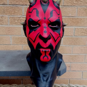 May include: A red and black mask with horns and a detailed face design. The mask is made of a hard plastic material and is a popular collectible for fans of the Star Wars franchise.