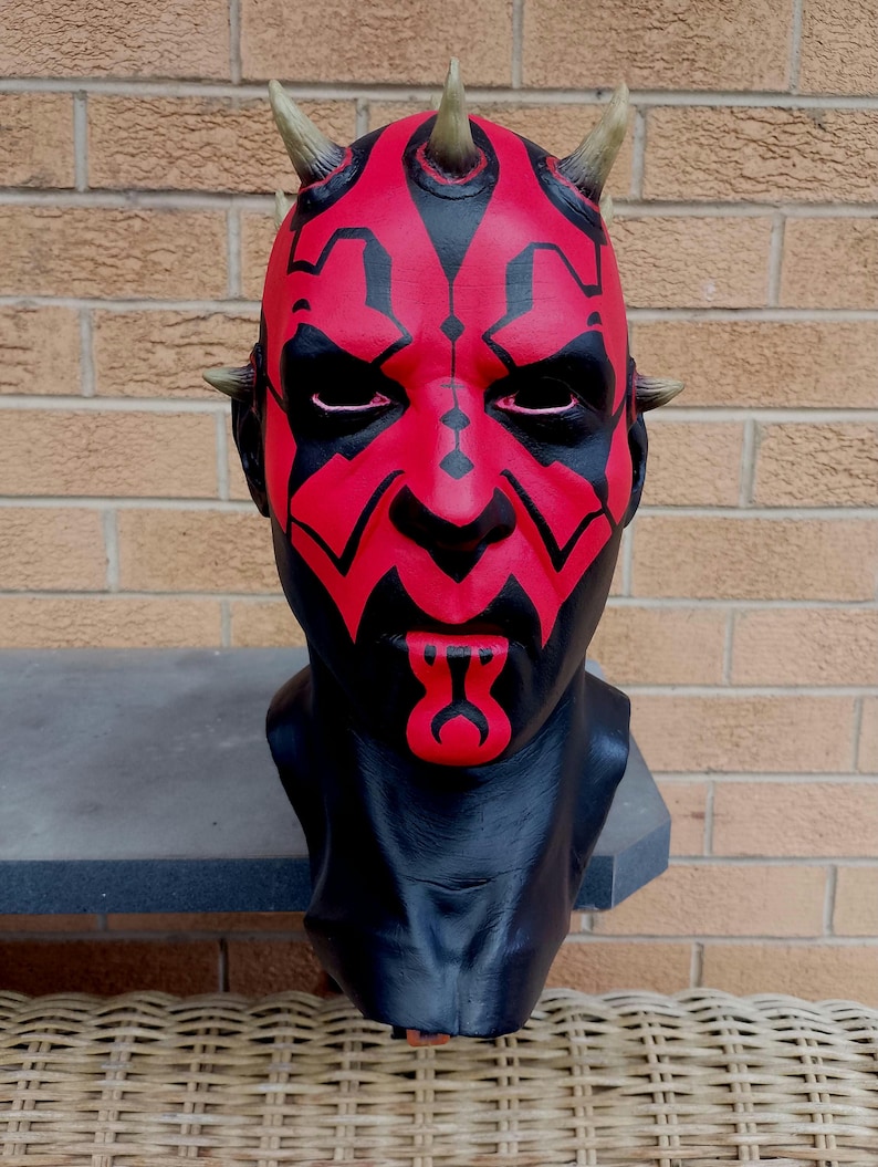 May include: A red and black mask with horns and a detailed face design. The mask is made of a hard plastic material and is a popular collectible for fans of the Star Wars franchise.