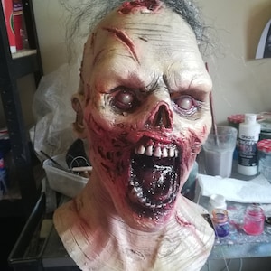 May include: A detailed, realistic zombie mask with a gaping mouth, exposed teeth, and blood-red wounds. The mask is made of a flesh-toned material and has a realistic texture.