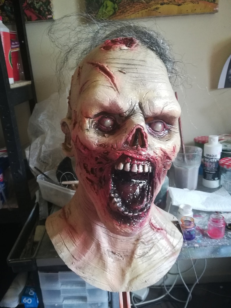 May include: A detailed, realistic zombie mask with a gaping mouth, exposed teeth, and blood-red wounds. The mask is made of a flesh-toned material and has a realistic texture.