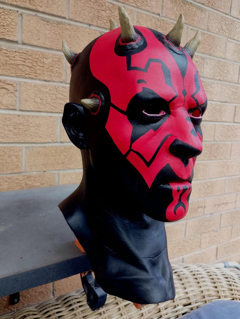 May include: A red and black Darth Maul mask with horns. The mask is made of plastic and has a detailed paint job.