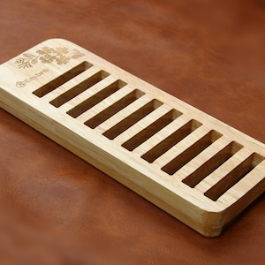 May include: Wooden storage rack with 10 slots for holding items like lip balm or small tubes of paint. The rack is made of light wood and has a floral design engraved on the top.