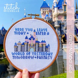 May include: A white cross-stitch embroidery hoop with a blue and pink castle design and the text "Here you leave today + enter a world of yesterday tomorrow + fantasy".