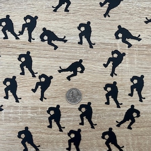 May include: Black paper cutouts of hockey players in various skating poses. The cutouts are scattered on a woodgrain surface.