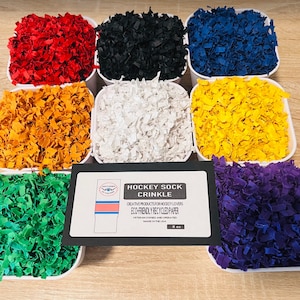 Może przedstawiać: Zestaw kolorowego, posiekanego papieru w białych pojemnikach. Papier jest wykonany z materiałów pochodzących z recyklingu i jest przyjazny dla środowiska. Papier jest oznaczony jako "Hockey Sock Crinkle" i jest kreatywnym produktem dla miłośników hokeja.