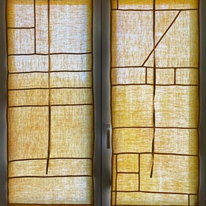 Peut inclure: Deux panneaux de fenêtre avec un motif géométrique. Les panneaux sont faits d'un tissu jaune clair avec des lignes marron foncé créant des formes rectangulaires et angulaires. Le cadre de la fenêtre est blanc, et l'esthétique générale est minimaliste et moderne.