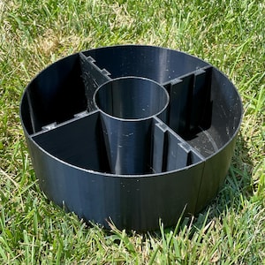 May include: A black, circular organizer with multiple compartments. The organizer is made of a solid material and is designed to hold and separate various items. It is sitting on a bed of green grass.