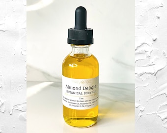 May include: A clear glass bottle with a black dropper top filled with a yellow liquid. The label reads "Almond Delight Botanical Body Oil 2 fl. oz.  Use desired amount to clean skin as often as desired. Sunflower Oil, Jojoba Oil, Argan Oil, Vitamin E Oil, Fragrance."