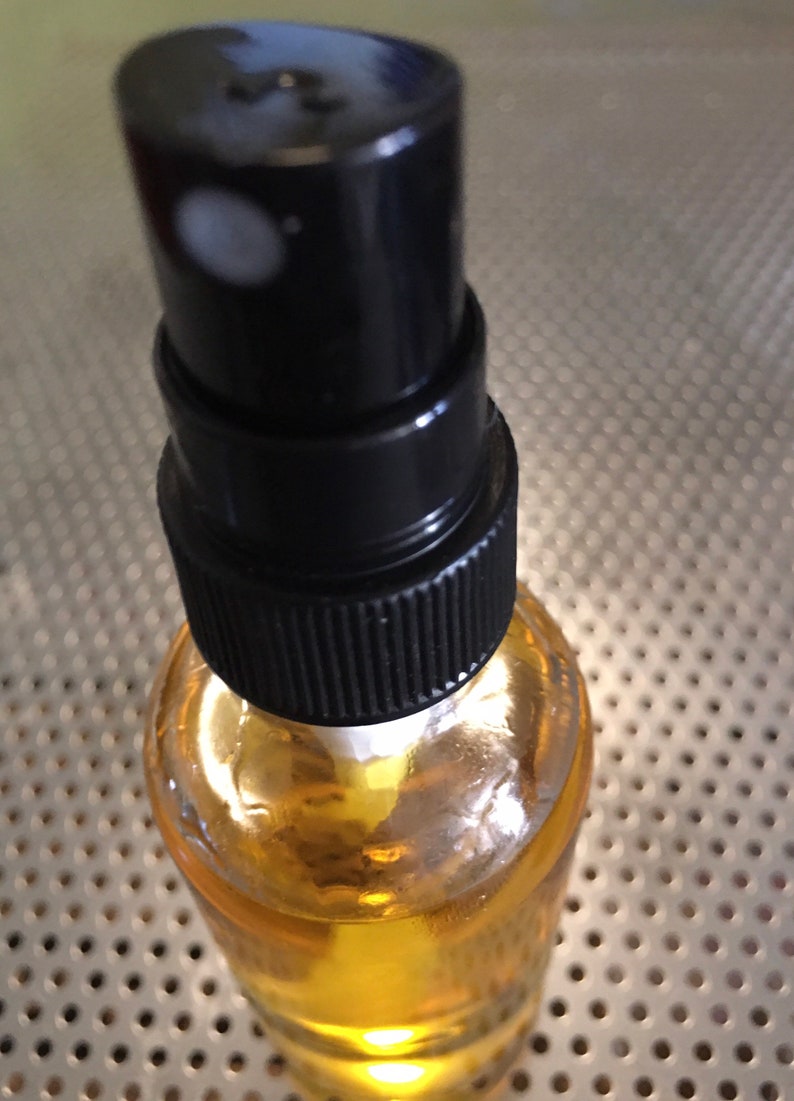 May include: A clear glass bottle with a black spray nozzle filled with a yellow liquid. The bottle is sitting on a silver surface with a pattern of small holes.