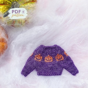 May include: A miniature purple sweater with orange jack-o'-lantern designs. The sweater is knit and has a round neckline. The words "PDF pattern" are in the upper left corner. The background is white and fluffy.