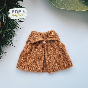May include: A brown knitted cape featuring a cable knit pattern and a button fastening. The cape has a collar and is made from a soft, textured yarn. The text "PDF pattern" is visible in the upper left corner.