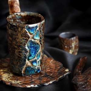 May include: A set of ceramic teacups and a teapot with a brown and blue glaze. The cups and teapot have a textured surface that resembles scales.