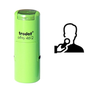 May include: A light green Trodat printy 4612 stamp with a clear top. Next to the stamp is a black and white graphic of a person being interviewed, with a microphone held up to their face.