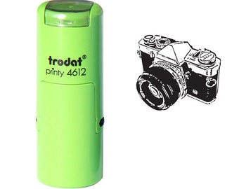 May include: A light green self-inking stamp with the text "trodat printy 4612" next to a black and white illustration of a vintage camera. The stamp has a rounded rectangular shape.