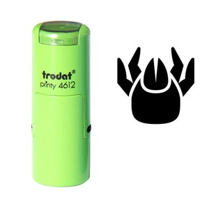 Puede incluir: Un sello Trodat printy 4612 verde claro con un icono de garrapata negro. El sello tiene un diseño rectangular y una tapa verde. El icono de garrapata es una forma negra estilizada con un cuerpo redondeado y patas puntiagudas.
