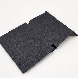 May include: A textured, black rectangular component with two cut-out sections and a slightly raised edge. The item appears to be made of a durable material and is set against a white background.