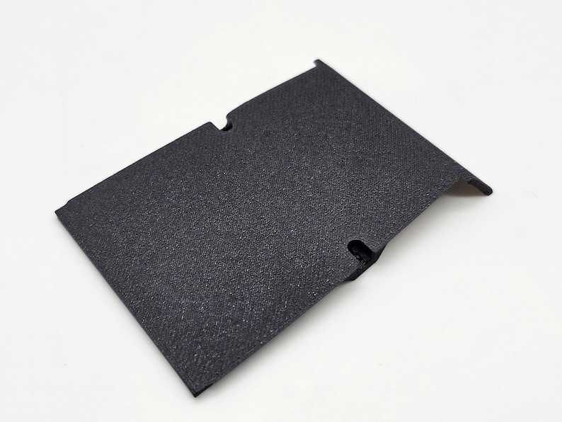 May include: A textured, black rectangular component with two cut-out sections and a slightly raised edge. The item appears to be made of a durable material and is set against a white background.