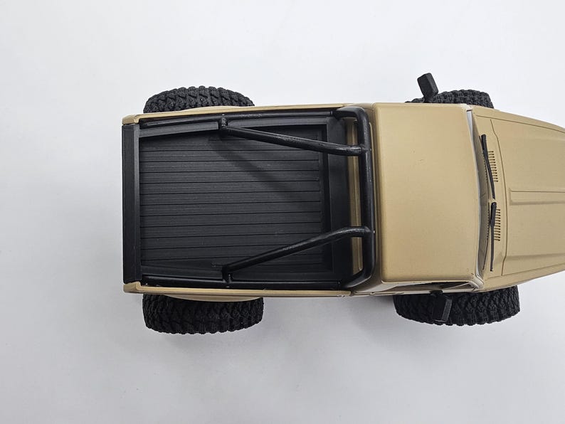 May include: Tan-colored toy pickup truck with black tires and a black roll bar. The truck bed is black with horizontal grooves. The tires are large and have a rugged tread pattern. The vehicle is viewed from above.