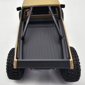 May include: Tan-colored toy pickup truck with black roll cage and black bed. The truck has large, black, off-road tires. The bed of the truck is black with vertical grooves. The truck is viewed from above.