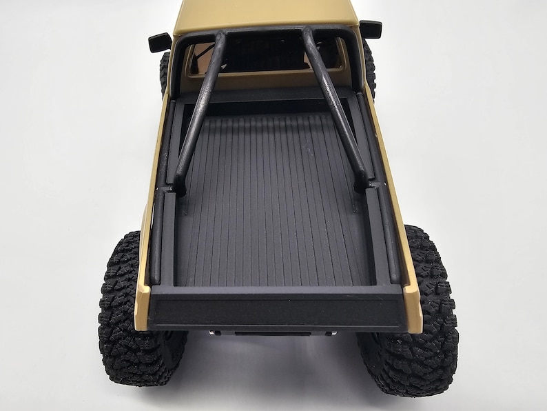 May include: Tan-colored toy pickup truck with black roll cage and black bed. The truck has large, black, off-road tires. The bed of the truck is black with vertical grooves. The truck is viewed from above.