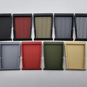 May include: A collection of ten wooden trays in various colors. The trays have a rectangular shape with vertical slats and a black frame. Colors include black, red, yellow, purple, gray, red, green, and beige.