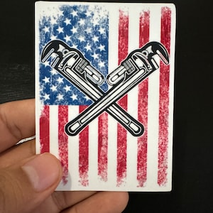 May include: A sticker with a distressed American flag design featuring two crossed wrench tools. The flag is red, white, and blue with a grunge effect.
