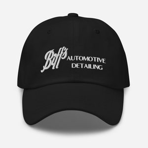 May include: Black baseball cap with white embroidered text reading "Biff's Automotive Detailing". The cap features a curved peak and a button on top. The text is in a cursive font.