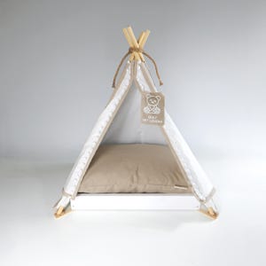 Può includere: Un teepee per animali domestici bianco e beige con un cuscino beige all'interno. Il teepee ha una struttura in legno ed è decorato con un'etichetta con la scritta "ONLY PET LOVERS" e una grafica di un orsacchiotto. Progettato per piccoli animali.