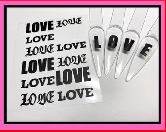 May include: A sheet of white paper with the word "LOVE" printed in black in different fonts and styles. There are five clear plastic nail tips with the word "LOVE" printed on them in black.