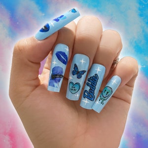 May include: Blue and white long acrylic nails with various designs including a butterfly, a heart with the text "Oh Okay", a smiley face, and the text "Baddie".