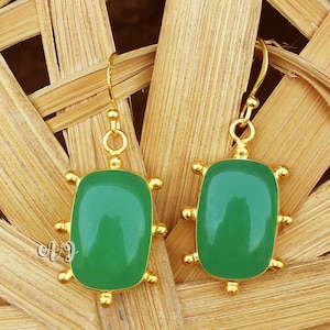 May include: A pair of gold earrings with green gemstone accents. The earrings feature a square-shaped gemstone set in a gold frame with decorative accents.
