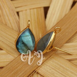 May include: A pair of gold teardrop earrings with a blue-green labradorite gemstone. The earrings have a post back.