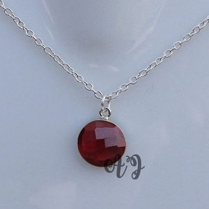 May include: A silver chain necklace with a round, red gemstone pendant.