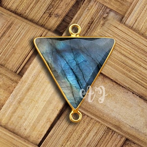 Puede incluir: Pendiente de triángulo de oro con una piedra preciosa de labradorita azul. El pendiente tiene dos anillos de salto para sujetarlo a un collar o pulsera.