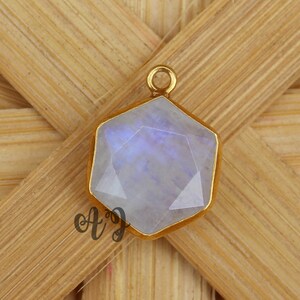 May include: A gold-toned pendant with a hexagonal moonstone gemstone. The stone is iridescent and has a light blue hue.