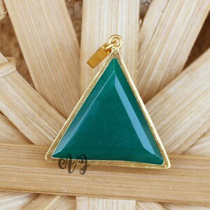 Op de afbeelding: Een gouden hanger met een driehoekige groene edelsteen. De hanger ligt op een houten oppervlak.