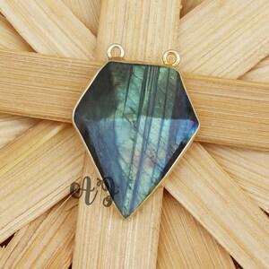 May include: A gold-toned pendant featuring a dark green and blue gemstone with iridescent shimmer. The gemstone is cut in a diamond shape and has a smooth, polished finish.