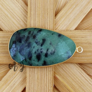 Könnte beinhalten: Ein grüner und schwarzer Edelstein-Anhänger mit einer goldenen Öse. Der Edelstein ist oval geformt und hat ein geflecktes Muster.