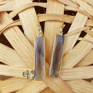 May include: A pair of gold dangle earrings with rectangular, clear smoky quartz stones.