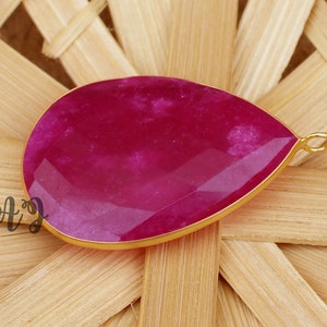 May include: A teardrop-shaped pendant with a pink gemstone set in gold.