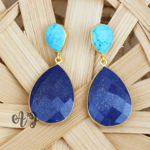 Peut inclure: Boucles d'oreilles dorées avec une pierre supérieure turquoise et une pierre inférieure en forme de goutte d'eau, facettée, bleu foncé. Présentées sur une surface tissée brun clair.