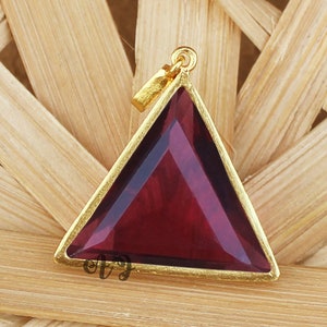 May include: Gold-tone pendant featuring a triangular shaped red gemstone.