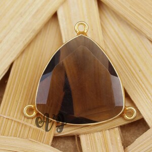 May include: Gold-tone triangle pendant with a smoky quartz gemstone. The pendant has three jump rings for attaching to a chain or cord.