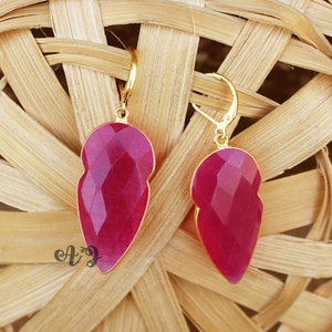 Könnte beinhalten: Ein Paar goldene Ohrringe mit rosafarbenen Edelstein-Tropfen. Die Ohrringe haben eine Tropfenform und sind in einer goldenen Fassung gefasst.