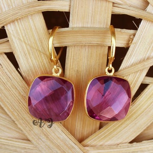 Può includere: Un paio di orecchini d'oro con pietre preziose viola di forma quadrata. Gli orecchini sono pendenti e hanno un design ad anello.