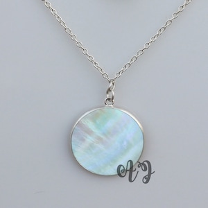 Puede incluir: Un collar de cadena de plata con un colgante redondo con una incrustación de nácar blanco y azul iridiscente.