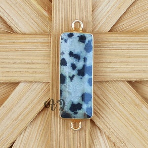 Op de afbeelding: Een rechthoekige hanger van zwart-witte dalmatijnse jaspis met een gouden metalen beugel.