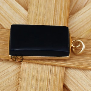 May include: A black onyx gemstone pendant with a gold-toned bail. The pendant is rectangular in shape and has a smooth, polished finish.